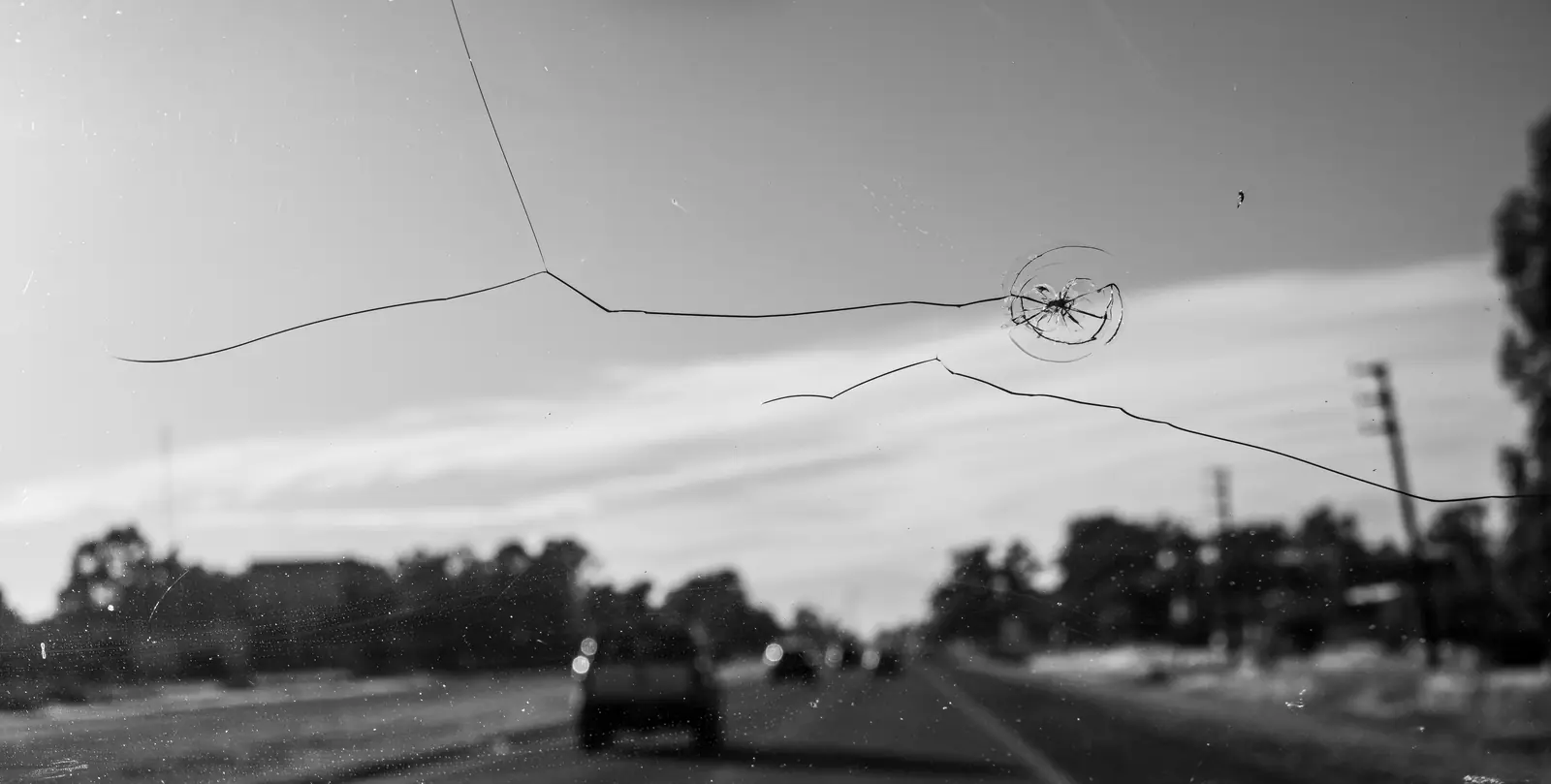 A long crack and a chip across a windshield, seen from inside a car on the road