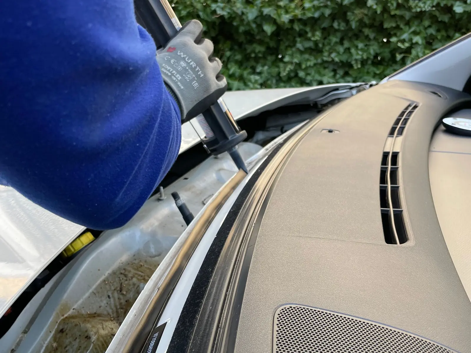 A gloved hand laying a bead of adhesive along a car’s windshield frame, with the glass out
